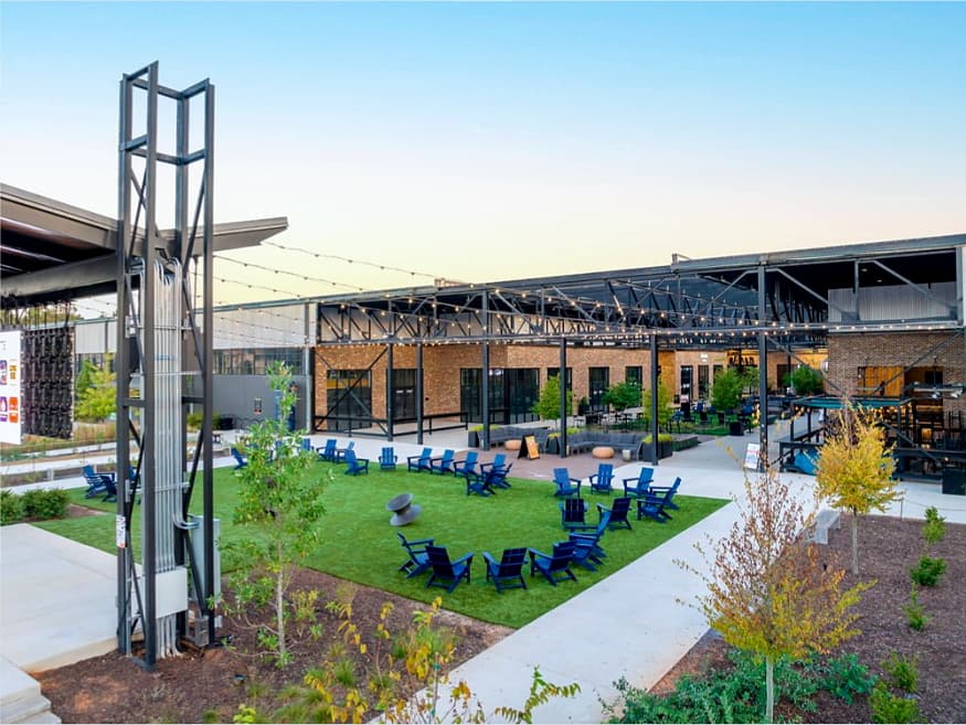 The courtyard at Wire Park in Watkinsville, Georgia, at dusk — a brick factory conversion with a steel canopy and festoon lighting